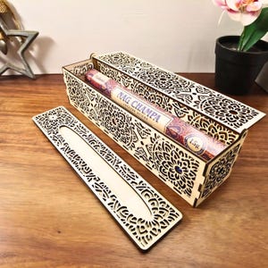 Op de afbeelding: Houten wierookdoos met ingewikkelde lasergesneden bloempatronen. De doos is open en onthult een Nag Champa wierookstokjesverpakking. Het deksel en een aparte wierookhouder zijn ook zichtbaar, allemaal in een natuurlijke houten afwerking.