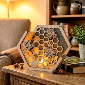 May include: A wooden, hexagonal candle holder with a honeycomb design and three laser-cut bee decorations. The interior glows with warm light from a lit candle, creating a cozy ambiance. The holder is placed on a wooden table.