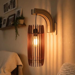 May include: A wooden wall sconce with a cylindrical shade made of vertical wooden slats. The sconce has a warm, inviting glow from the exposed lightbulb. The fixture is mounted on a curved wooden arm attached to the wall, creating a modern, rustic aesthetic.