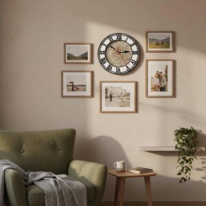 May include: A wall decor arrangement featuring a large round clock with Roman numerals and a decorative center, surrounded by framed photographs. The clock has a black frame and a white face with a detailed design. The frames are a light brown color.