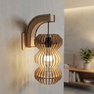 May include: Wooden wall-mounted light fixture with a unique, layered design. The light has a curved wooden arm and a shade composed of vertical wooden slats. The light is turned on, illuminating the interior of the shade. The fixture is mounted on a light-colored wall.