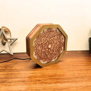 Peut inclure: Lampe octogonale en bois avec un motif mandala découpé au laser. L'intérieur est clair et l'extérieur est marron. Le motif complexe est un point central, ajoutant une touche artistique à la décoration.