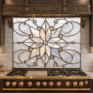 May include: A kitchen backsplash with a floral design made of iridescent glass and crystal embellishments. The backsplash is above a dark brown stove with gold-coloured knobs and a matching range hood. The kitchen features dark brown cabinets.