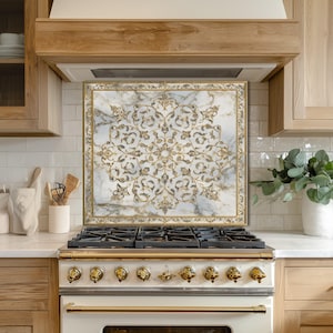 Pode incluir: Uma proteção contra respingos de cozinha com um design semelhante a mármore com um padrão floral dourado. A proteção contra respingos é emoldurada em dourado e fica acima de um fogão branco e dourado. A cozinha tem armários de madeira clara e azulejos brancos.