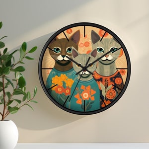 May include: A round wall clock with a black frame and a colorful design featuring three cats wearing sweaters and floral patterns. The clock face has black hands and Roman numeral markings.