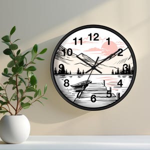 May include: Black and white wall clock with a mountain lake scene. The clock face features roman numerals and a black hand pointing to the number 12. The scene depicts a lake with a boat docked at a wooden pier, mountains in the background, and a pink sunset.