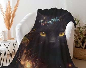 May include: A black throw blanket featuring a large, detailed illustration of a black cat with bright yellow eyes. The cat is adorned with a delicate crown of small blue leaves and glowing golden light particles that swirl around its face.