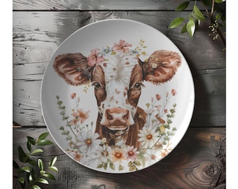 May include: White ceramic plate with a brown and white cow illustration wearing a flower crown. The cow is surrounded by watercolor flowers and greenery.