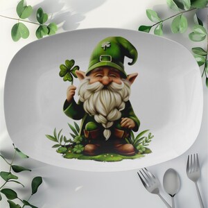 May include: White oval serving platter with a green leprechaun holding a four-leaf clover. The leprechaun is wearing a green hat with a gold buckle and a green beard.