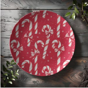 May include: A round red plate with a repeating pattern of white and red candy canes and white snowflakes. The candy canes have white bows. The plate is on a wooden surface.
