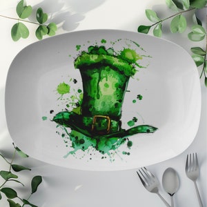 May include: A white oval serving platter with a green leprechaun hat design. The hat is painted in a watercolor style with green, white, and gold accents. The hat is surrounded by green splatters.