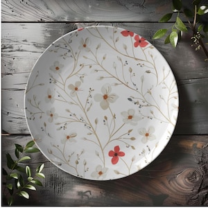 May include: White ceramic plate with a floral design. The plate features a pattern of delicate white flowers, tan stems, and pops of red flowers. The plate is round and sits on a wooden surface.
