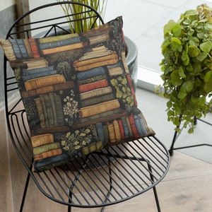 May include: A black metal chair with a cushion featuring a pattern of stacked books and greenery. The cushion is a dark blue color with brown, red, and yellow accents. The chair is sitting on a light brown tiled floor.