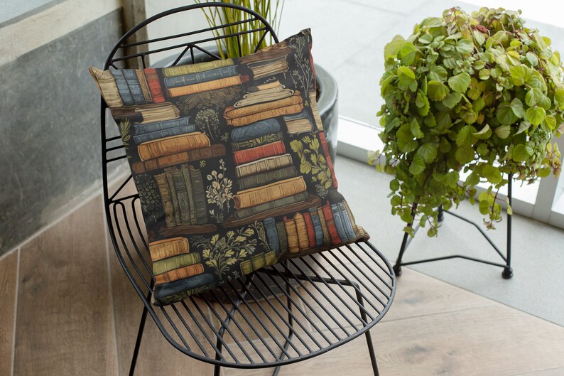 May include: A black metal chair with a cushion featuring a pattern of stacked books and greenery. The cushion is a dark blue color with brown, red, and yellow accents. The chair is sitting on a light brown tiled floor.