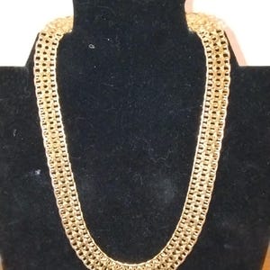 May include: A gold chain necklace with a thick, intricate design. The chain is made of multiple rows of linked metal pieces.