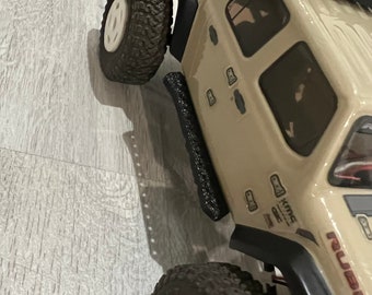 May include: A tan and black toy Jeep Wrangler with black side steps and the word "RUBICON" printed on the side. The Jeep has black wheels with white rims and a black roof.