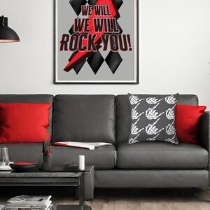 May include: A gray leather sofa with two red throw pillows and a gray throw pillow with a white skeleton hand pattern. The sofa is in front of a gray wall with a framed print that says "We Will Rock You!" in red and black letters.