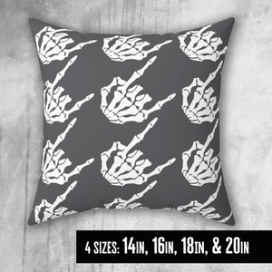 May include: A gray throw pillow with a white skeleton hand pattern. The hand is making a middle finger gesture. The pillow is available in four sizes: 14 in, 16 in, 18 in, and 20 in.
