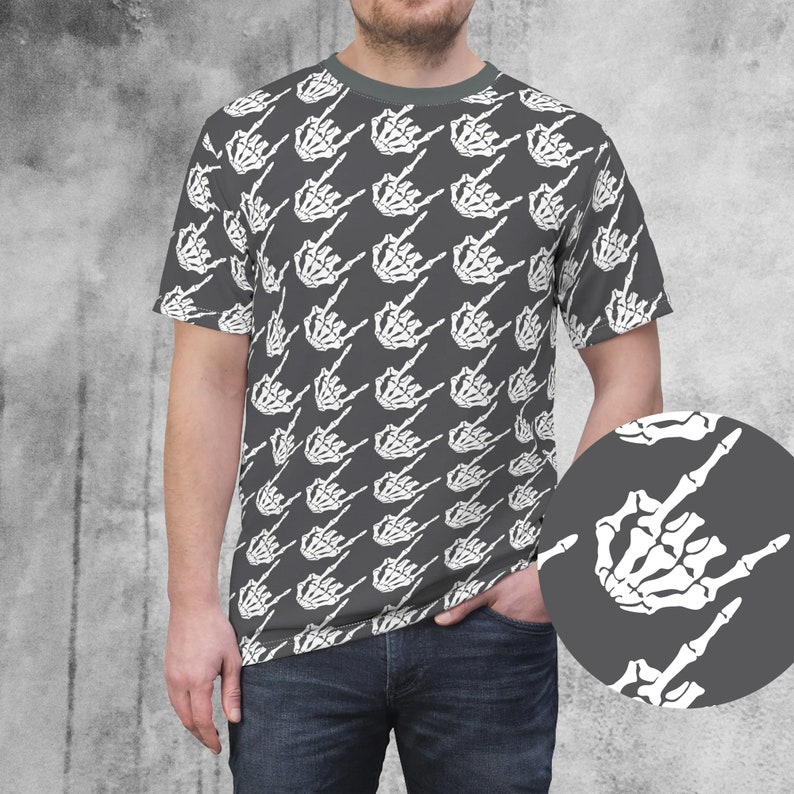 May include: Gray t-shirt featuring a repeating pattern of white skeleton hands making the rock on gesture. The shirt has a crew neck and short sleeves. A close-up of the hand gesture is in the lower right corner.