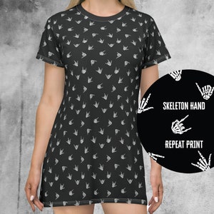 May include: Black t-shirt dress with a white skeleton hand print pattern. The print is repeated all over the dress. The dress has short sleeves and a round neckline. "Skeleton Hand Repeat Print" is written in white text on a black circle.