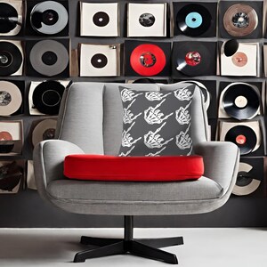 May include: A gray armchair with a red cushion and a throw pillow featuring a white skeleton hand making a middle finger gesture on a gray background.