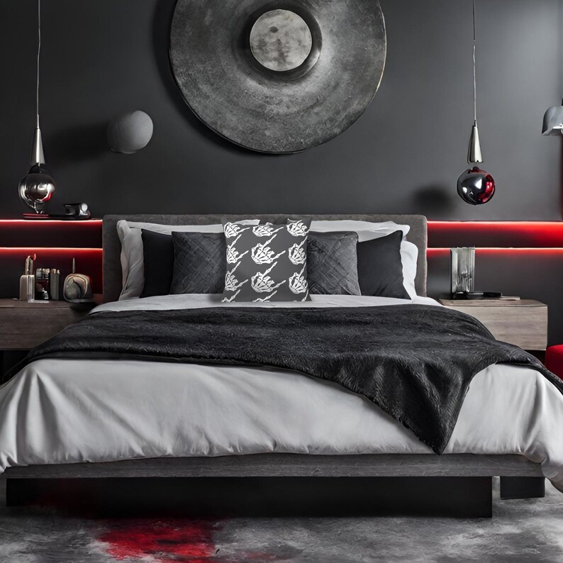 May include: A gray bed with a black throw blanket and a decorative pillow with a white skeleton hand design. The bed is in a dark room with a large, round, silver wall decoration.