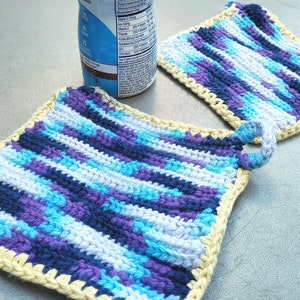 May include: Two crocheted pot holders with a yellow border. One pot holder has a loop handle. The pot holders are striped with blue, purple, and white yarn.
