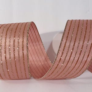 May include: A wide, dusty pink ribbon featuring vertical stripes of shimmering copper glitter. The edges of the ribbon are finished with a thin, metallic copper trim, and the fabric has a smooth, satin-like texture with a consistent repeating pattern.
