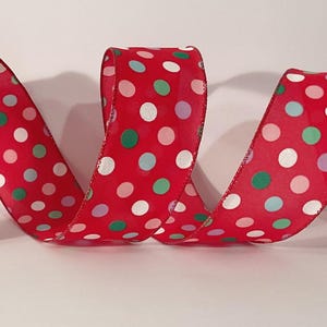 Puede incluir: Cinta roja con un patrón de lunares blancos, acentuada con puntos verdes, celeste y morados. La cinta está rizada y se muestra sobre una superficie blanca. Esta cinta decorativa es adecuada para manualidades y envolver regalos.