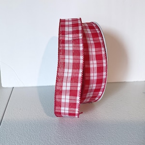 May include: A roll of red and white checked ribbon. The ribbon features a traditional gingham pattern with a white base and red squares. The edges are finished with a decorative red trim. Ideal for crafts and gift wrapping.