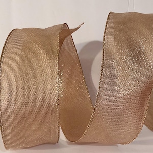 May include: A metallic gold ribbon with a shimmering, textured surface and a woven appearance. The ribbon features a structured, wired edge in a matching gold tone, allowing it to hold its shape in a loose, spiralling, and undulating form.