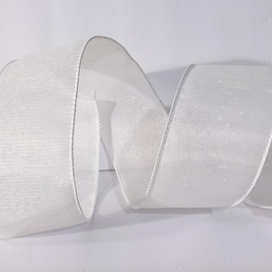 May include: A wide, solid white ribbon with a woven, semi-sheer texture and finished edges. The ribbon is arranged in a loose, flowing S-curve shape, showcasing its consistent colour and light-reflecting surface across the entire length of the fabric.
