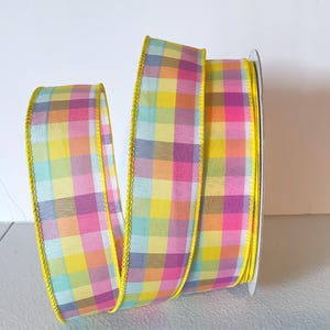 May include: A spool of colorful plaid ribbon. The ribbon features a pattern of yellow, pink, purple, and blue squares. The edges are trimmed with a yellow border. This decorative ribbon is suitable for crafts and gift wrapping.