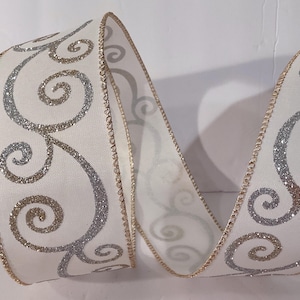 May include: A white ribbon featuring a repeating pattern of swirling filigree designs in alternating silver and gold glitter. The edges of the ribbon are finished with a metallic gold thread border, creating a structured and decorative appearance.