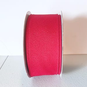 May include: A roll of red ribbon with a textured surface. The ribbon is wrapped around a white cardboard spool. The ribbon is a solid, vibrant red colour.