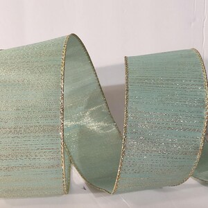 May include: A wide, light mint green ribbon featuring a subtle horizontal metallic texture and shimmering gold-toned edges. The ribbon is arranged in a series of loose, flowing loops, showcasing its smooth, reflective surface and structured, wired borders.