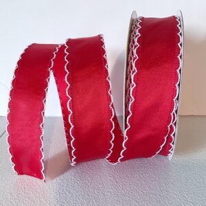 May include: A reel of red ribbon with a white, scalloped edge. The ribbon is unrolled, displaying its texture and design. This decorative ribbon is suitable for crafts, gift wrapping, and other creative projects.