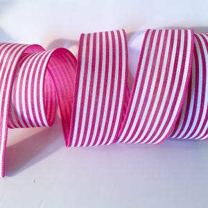 Può includere: Un rotolo di nastro rosa acceso con strisce bianche verticali. Il nastro è arrotolato, mostrando il lato inferiore rosa e la parte superiore a righe bianche e rosa. I bordi sono rifiniti con un bordo cucito rosa.