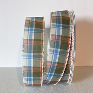May include: A roll of plaid ribbon in blue, green, orange, and cream. The ribbon has a stitched edge and is suitable for crafting, gift wrapping, or decoration. The ribbon is on a white spool.