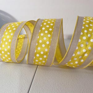 May include: A roll of decorative ribbon with a yellow background and white polka dots. The ribbon has a tan border and is curled in a spiral shape. This ribbon is suitable for crafts, gift wrapping, and decorations.