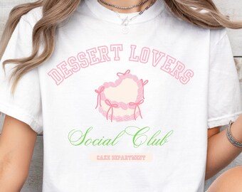 May include: White t-shirt with a pink and green graphic that says "Dessert Lovers Social Club Cake Department".