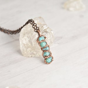 May include: A copper necklace with a pendant made of turquoise stones. The stones are set in a spiral pattern and are a light blue color. The necklace is on a white surface.