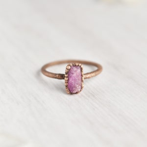 May include: A copper ring with a raw pink gemstone set in a textured band.