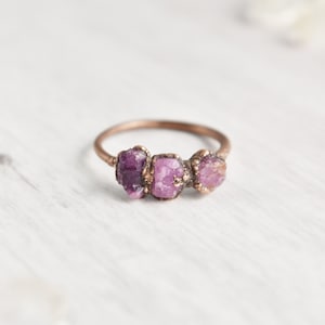 May include: A copper ring with three small, raw, purple gemstones set in the band.