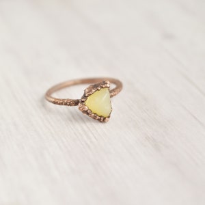 May include: A copper ring with a triangular yellow gemstone set in a textured copper setting.