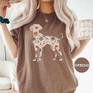 May include: Espresso-colored t-shirt featuring a floral dog design. The dog silhouette is filled with a pattern of peach and blue flowers. The shirt has a relaxed fit and is made of soft material.