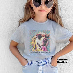 May include: A gray heather t-shirt with a graphic of a golden retriever wearing sunglasses and the text "In My Golden Era".