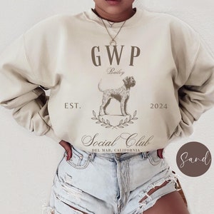 May include: A beige sweatshirt with a brown graphic design featuring a dog, the text "GWP", "Bailey", "EST. 2024", and "Social Club DEL MAR, CALIFORNIA".