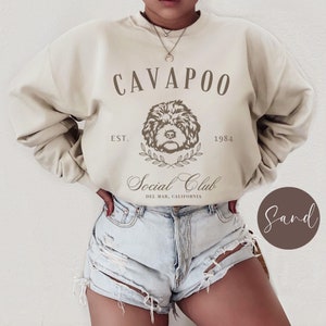 May include: A beige sweatshirt with the text "CAVAPOO Social Club EST. 1984 DEL MAR, CALIFORNIA" and a brown illustration of a cavapoo dog.