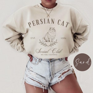 May include: A beige sweatshirt with the text "Persian Cat Est. 1984 Social Club Del Mar, California" and a drawing of a Persian cat.